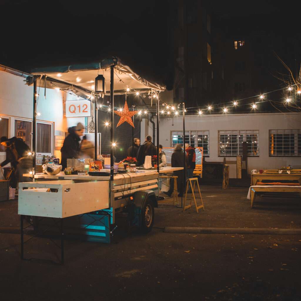 Beleuchtetes LIVIN’ROLL-Glühweinmobil mit Lichterketten bei Nacht im Hinterhof