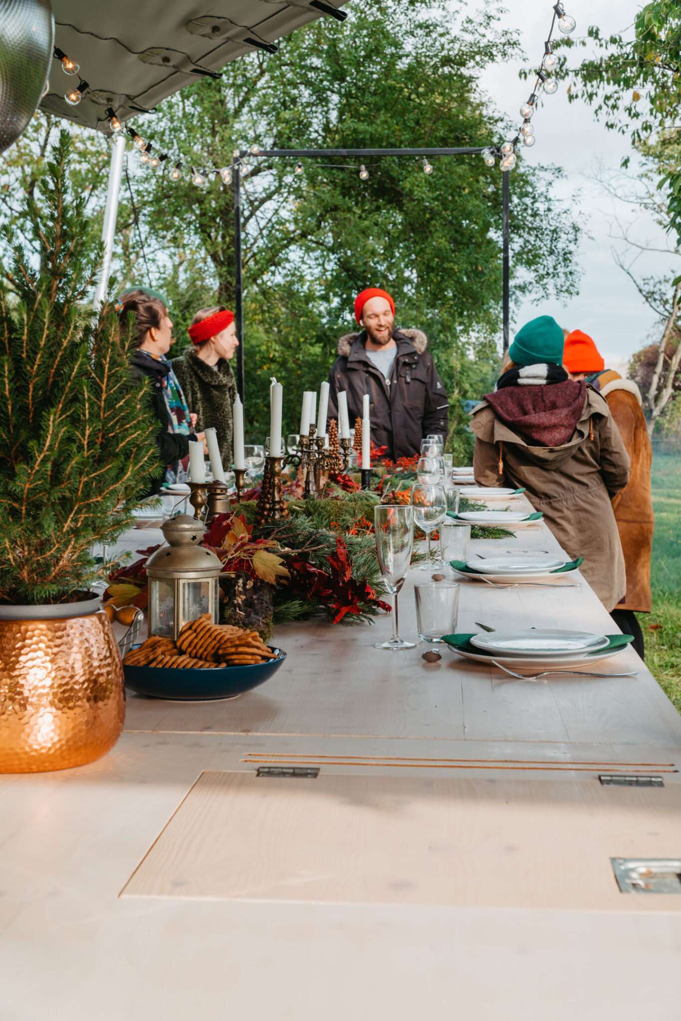 Gäste mit Wintermützen an einer festlich gedeckten langen Tafel im Grünen